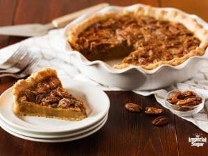 table with pecan pie with slice cut out and pecans on table