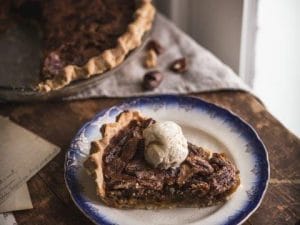 pecan pie slice with ice cream on a plate in front of a whole pecan pie