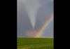 double rainbow in front of a tornado over a field of grass