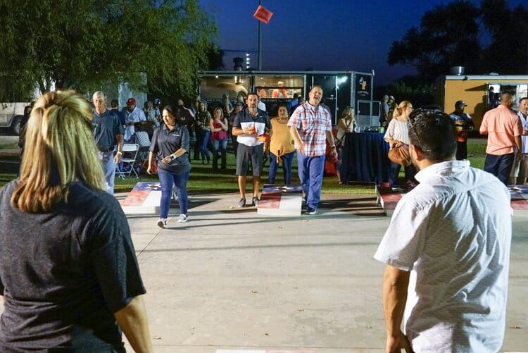 Texan people standing outside by food trucks playing a game of cornhole