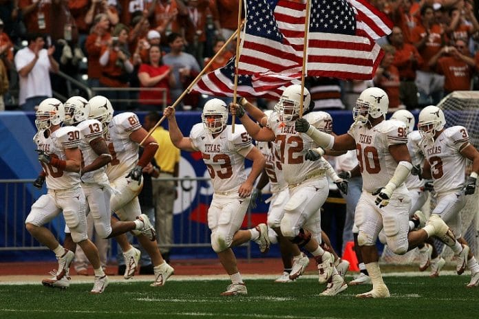 UT Austin football players on the field holding American flags