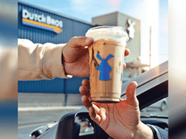 one person handing a Dutch Bros coffee to another person in a car outside of a Dutch Bros location