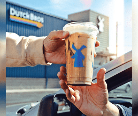 one person handing a Dutch Bros coffee to another person in a car outside of a Dutch Bros location