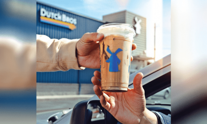 one person handing a Dutch Bros coffee to another person in a car outside of a Dutch Bros location