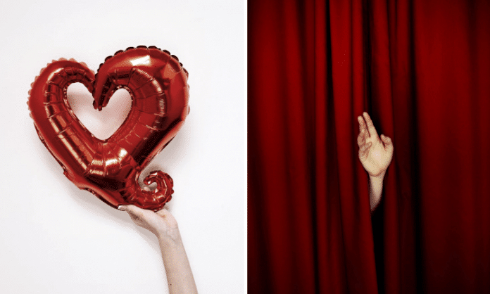 hand holding red heart balloon and hand waving through red stage curtain
