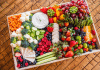 large tray charcuterie board filled with an array of fruits, vegetables, cheeses, and more