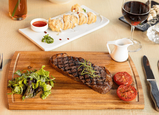 Chopping board of steak and tomatoes with a glass of wine.