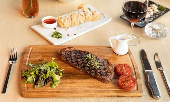 Chopping board of steak and tomatoes with a glass of wine.