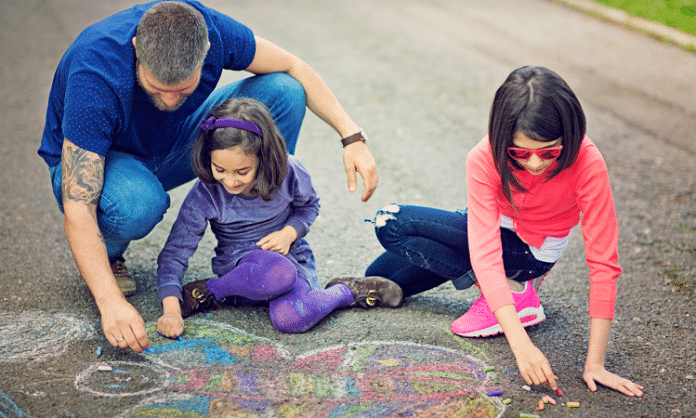 father and daughters making chalk art